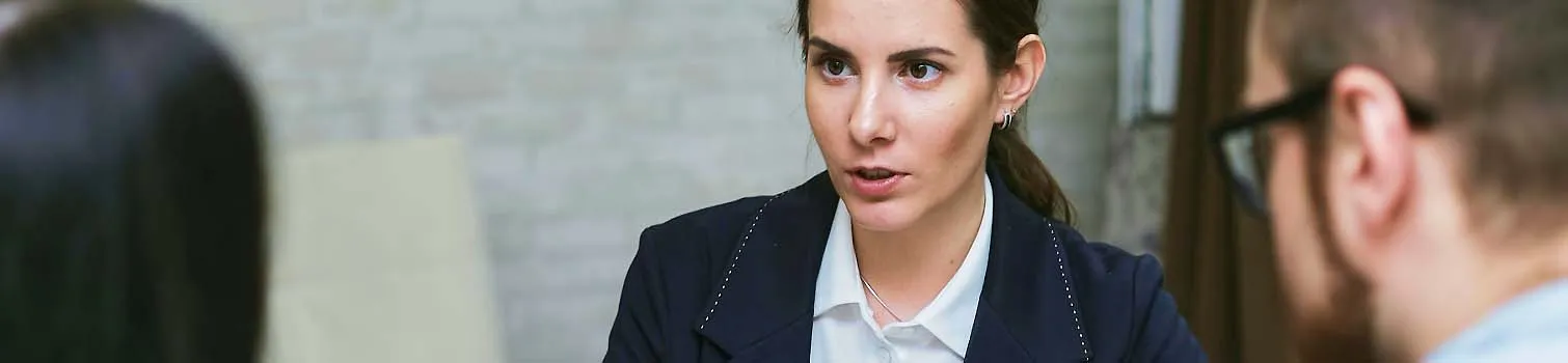 Frau im Business-Outfit spricht in einem Meeting mit zwei weiteren Personen.