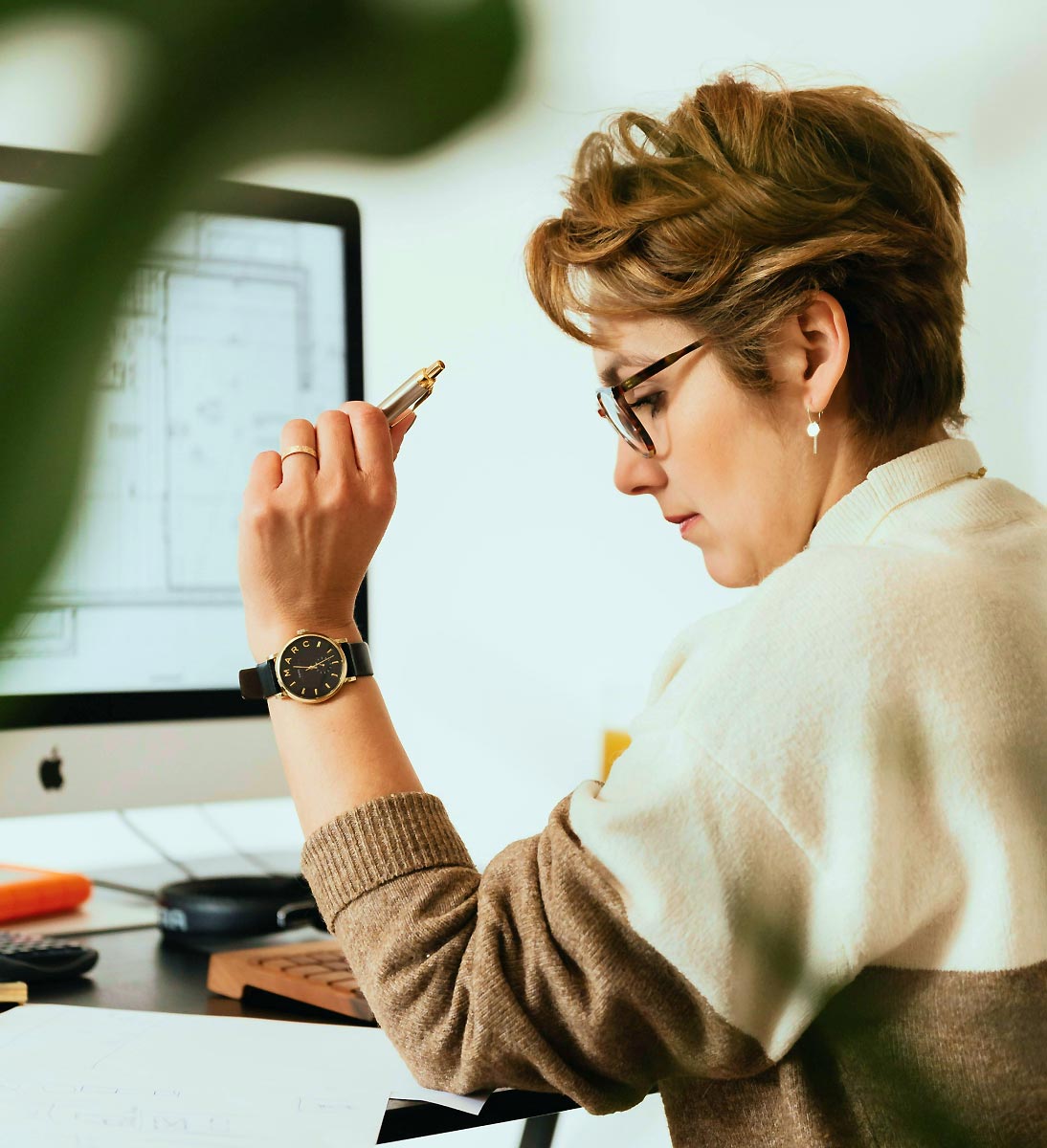 Frau mit Brille arbeitet konzentriert an einem Desktop-Computer und hält einen Stift in der Hand.