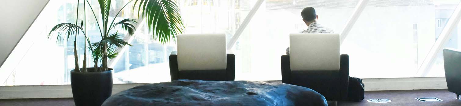 Person sitzt mit Laptop an einem Tisch vor großen Fenstern in einem modernen Büro.