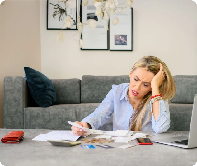 Frau sitzt am Tisch und prüft Rechnungen und Unterlagen mit Taschenrechner.