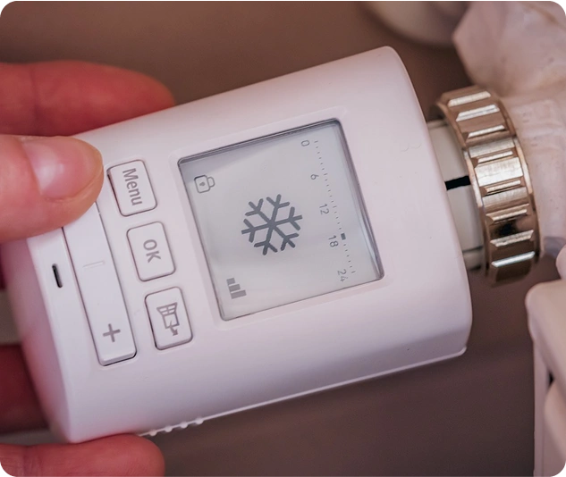 Hand stellt ein digitales Heizkörperthermostat mit Schneeflocken-Symbol ein.