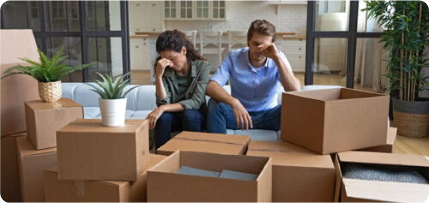 Paar sitzt zwischen Umzugskartons und wirkt erschöpft.