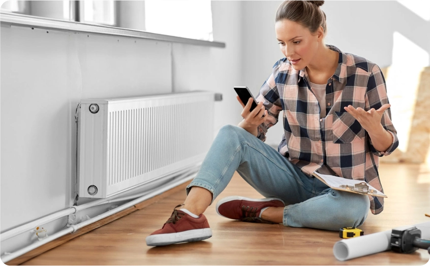 Frau sitzt auf dem Boden neben einem Heizkörper und telefoniert besorgt.