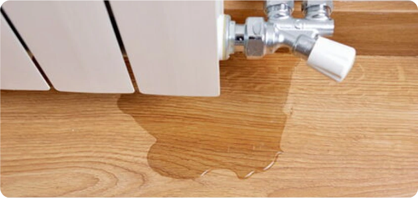 Wasser läuft aus einem Heizkörperventil und bildet eine Pfütze auf dem Boden.