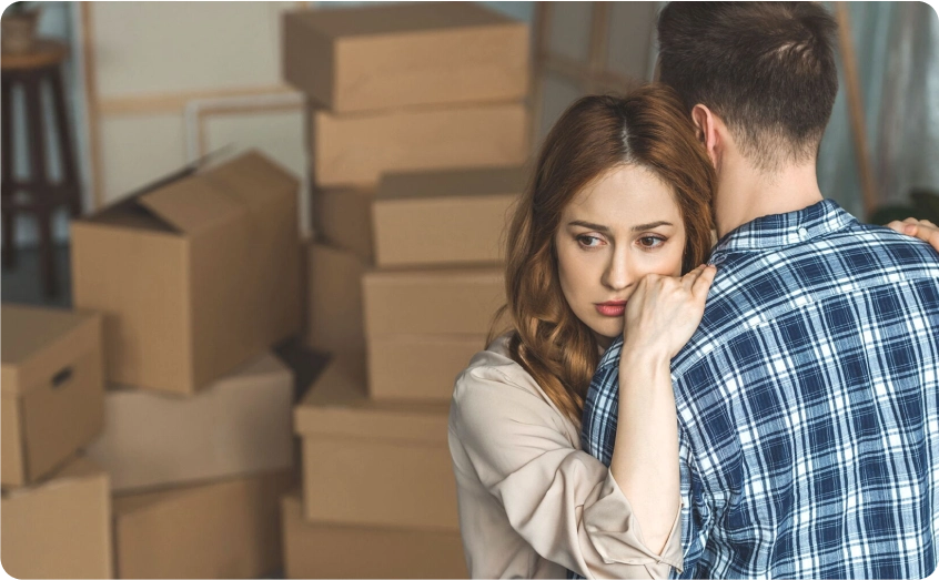 Frau lehnt sich besorgt an einen Mann, während Umzugskartons im Hintergrund stehen.
