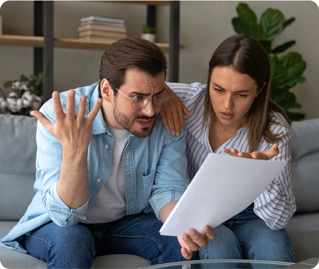 Paar sitzt auf dem Sofa und schaut besorgt auf ein Dokument.