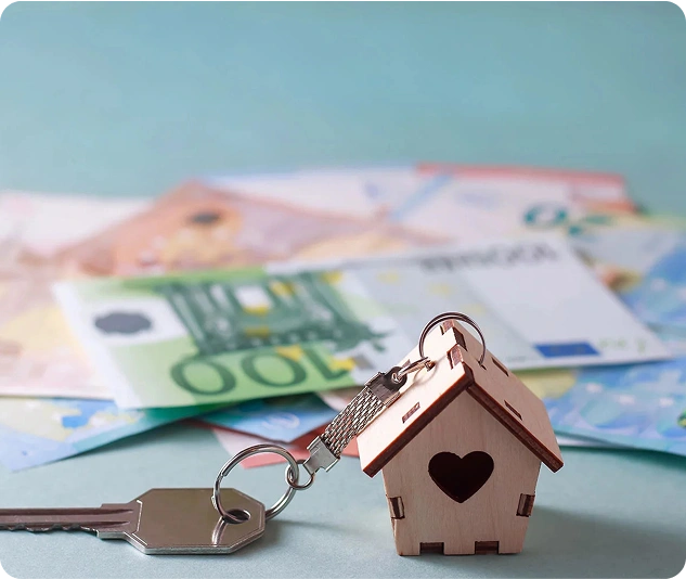 Hausschlüssel mit kleinem Hausanhänger liegen vor mehreren Euro-Banknoten.