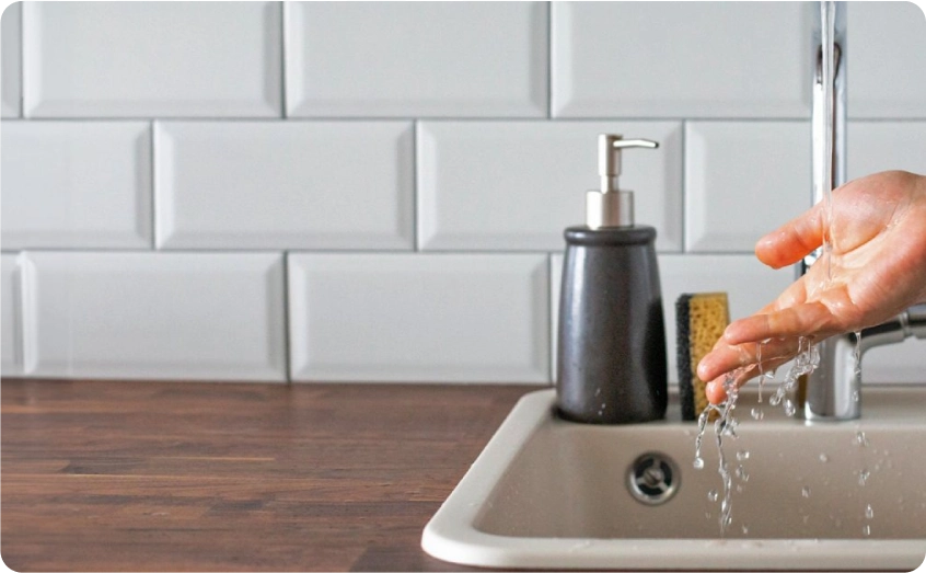 Hand hält Wasser aus einem Wasserhahn über einer Küchenspüle.