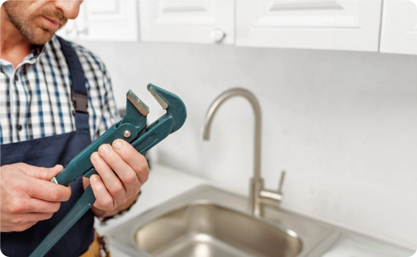 Handwerker hält eine Rohrzange vor einer Küchenspüle.