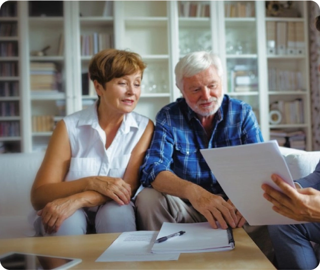 Älteres Paar sitzt am Tisch und bespricht Dokumente mit einer dritten Person.