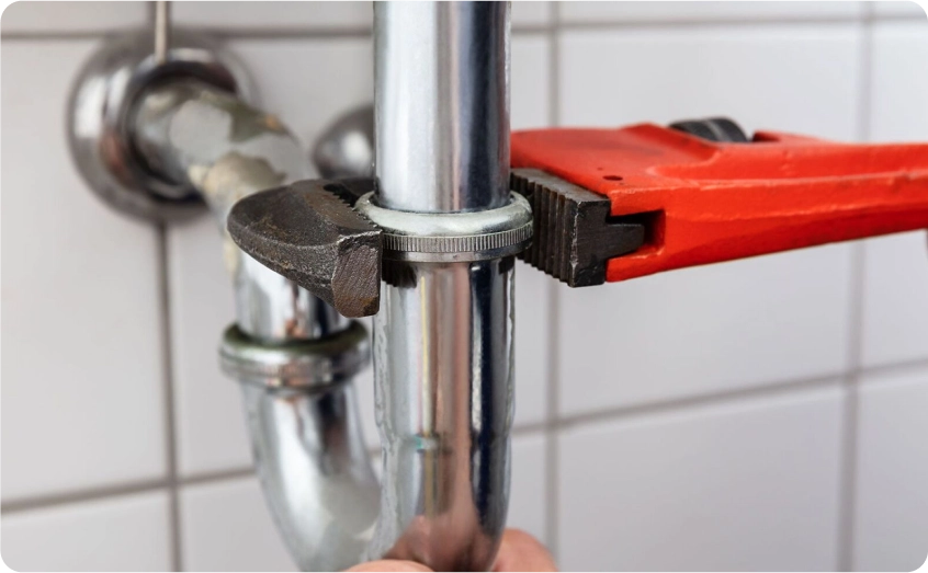 Rohrzange wird an einem Metallrohr unter einem Waschbecken angesetzt.