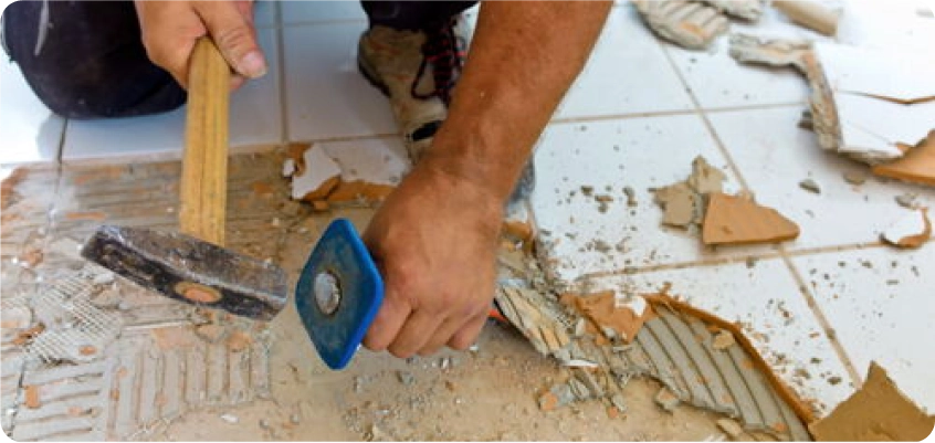 Handwerker entfernt alte Fliesen mit Hammer und Meißel vom Boden.