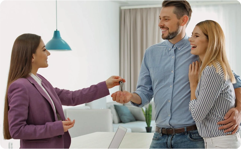 Frau übergibt einem Paar lächelnd einen Wohnungsschlüssel.