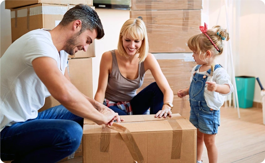Familie öffnet gemeinsam einen Umzugskarton in einer neuen Wohnung.