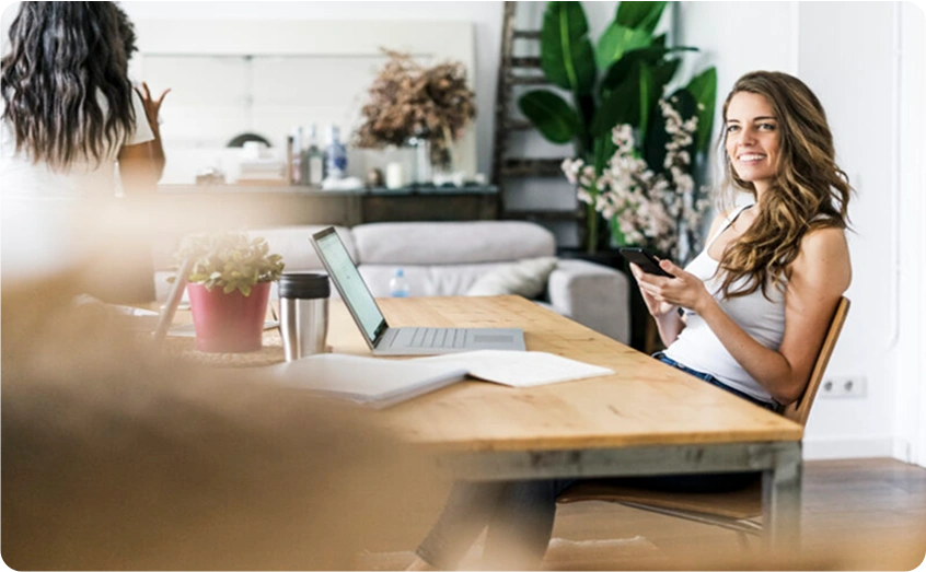 Frau sitzt entspannt am Tisch und nutzt ihr Smartphone.